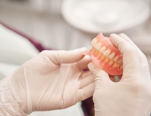 Gloved hands holding shiny new dentures