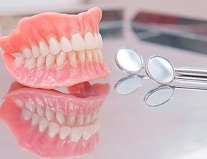 Closeup of complete set of dentures next to dental mirror on reflective surface