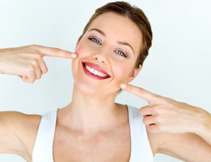 Woman with blue eyes pointing to her smile with both hands