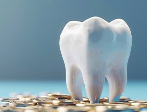 Large shiny model tooth on a pile of coins with blue-gray background