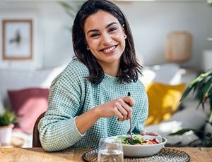 Woman with short hair smiling while eating salad at home