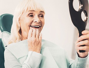 A woman admiring her dentures in a hand mirror