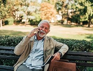 An older man talking on a cell phone while sitting on a park bench